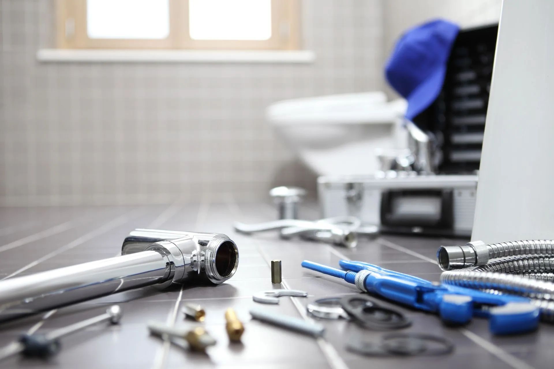 Plumbing tools on a bathroom floor, with a wrench, screwdrivers, and fittings near a sink.