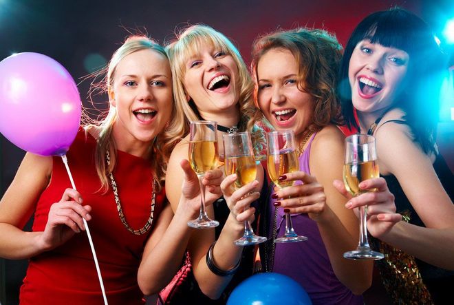 Group of women with balloons in front of a bus, laughing in a city street.