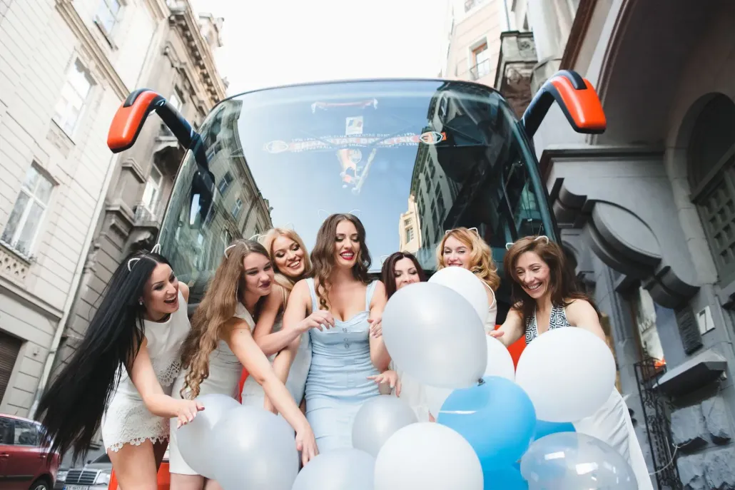 Group of women with balloons in front of a bus, laughing, outdoors.
