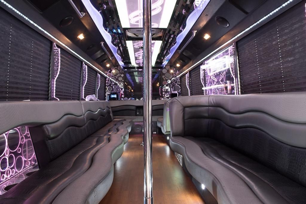 Interior of a luxury party bus with leather seating, a pole, and overhead lighting.