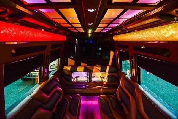 Interior of a party bus with colorful LED lighting, leather seats, and a bar area.
