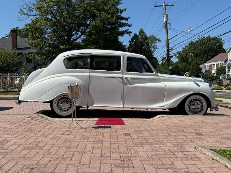 White vintage car parked on a brick driveway, with a red carpet in front.