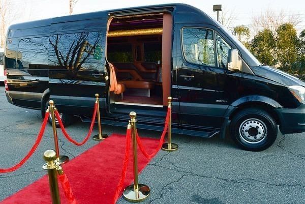 Black luxury van with open door, red carpet, and stanchions.