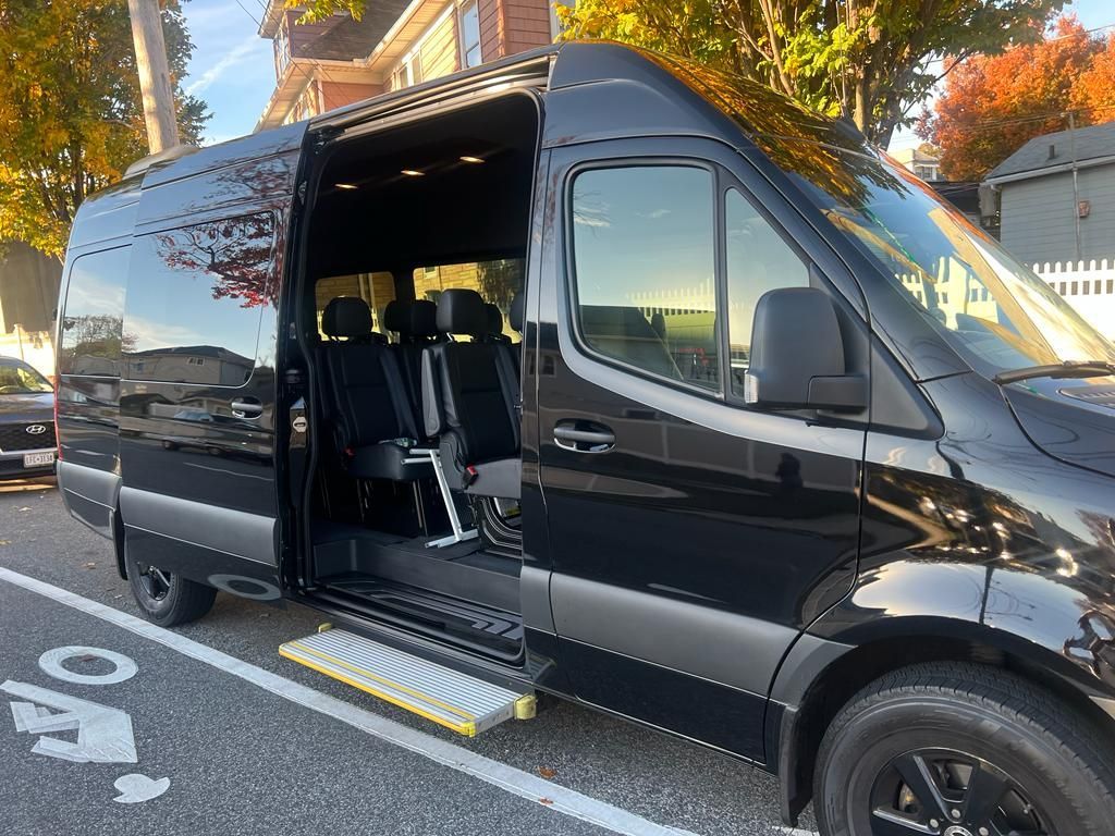 Black passenger van with open sliding door and accessible step. Parked on a street with bike lane.