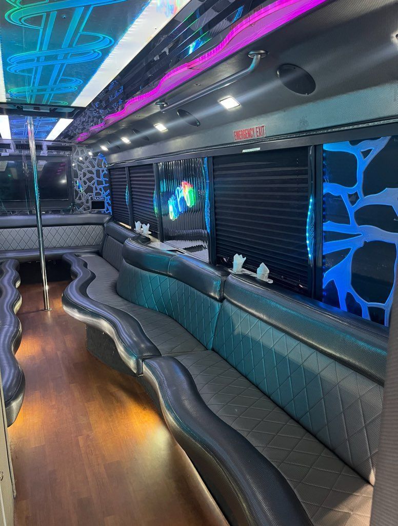 Interior of a party bus with black leather seating, wood floor, and neon lights.