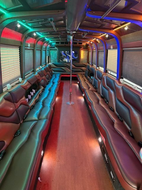 Interior of a party bus with leather seating, a dance pole, and colorful LED lighting.