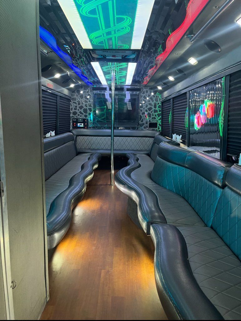Interior of a party bus with black and teal seating, a dance pole, and a mirrored ceiling with LED lights.