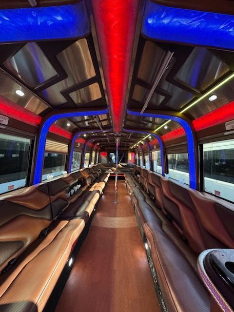 Interior of a party bus with brown leather seating, red and blue lights, and a wooden floor.
