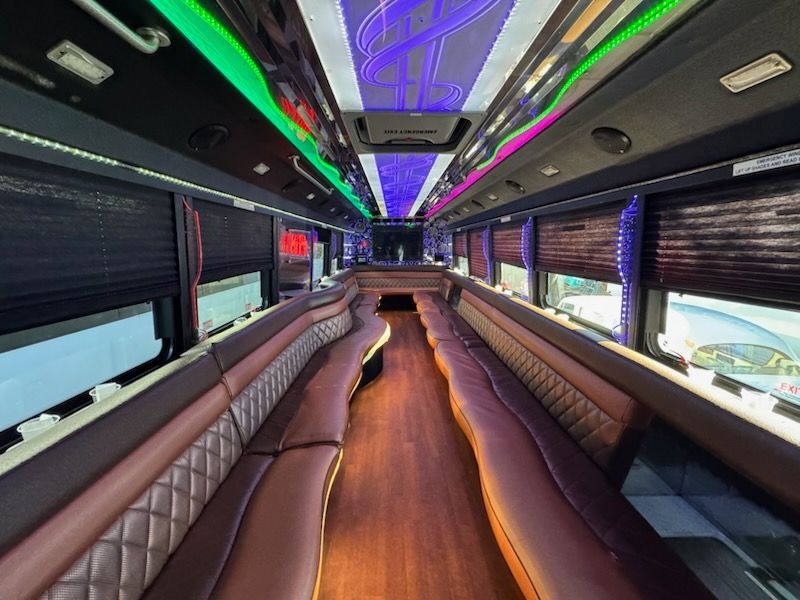 Interior of a luxury party bus with brown leather seating, wood floor, and colorful ceiling lights.