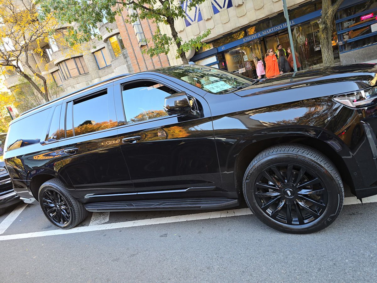Black SUV with black rims parked on city street. Buildings and people in the background.