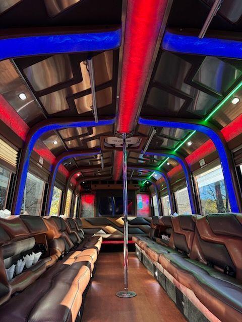 Interior of a party bus with leather seating, a dance pole, and neon lights along the ceiling.