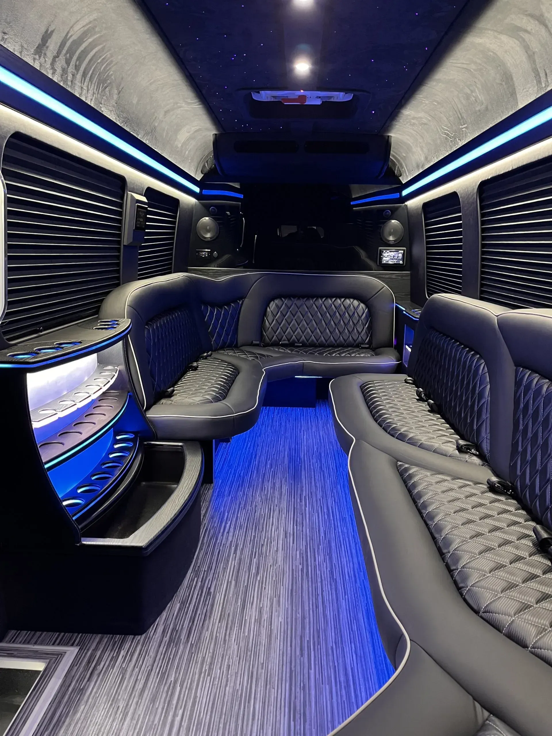 Luxurious, dark interior of a van. Blue LED lighting, tufted leather seating, bar area.