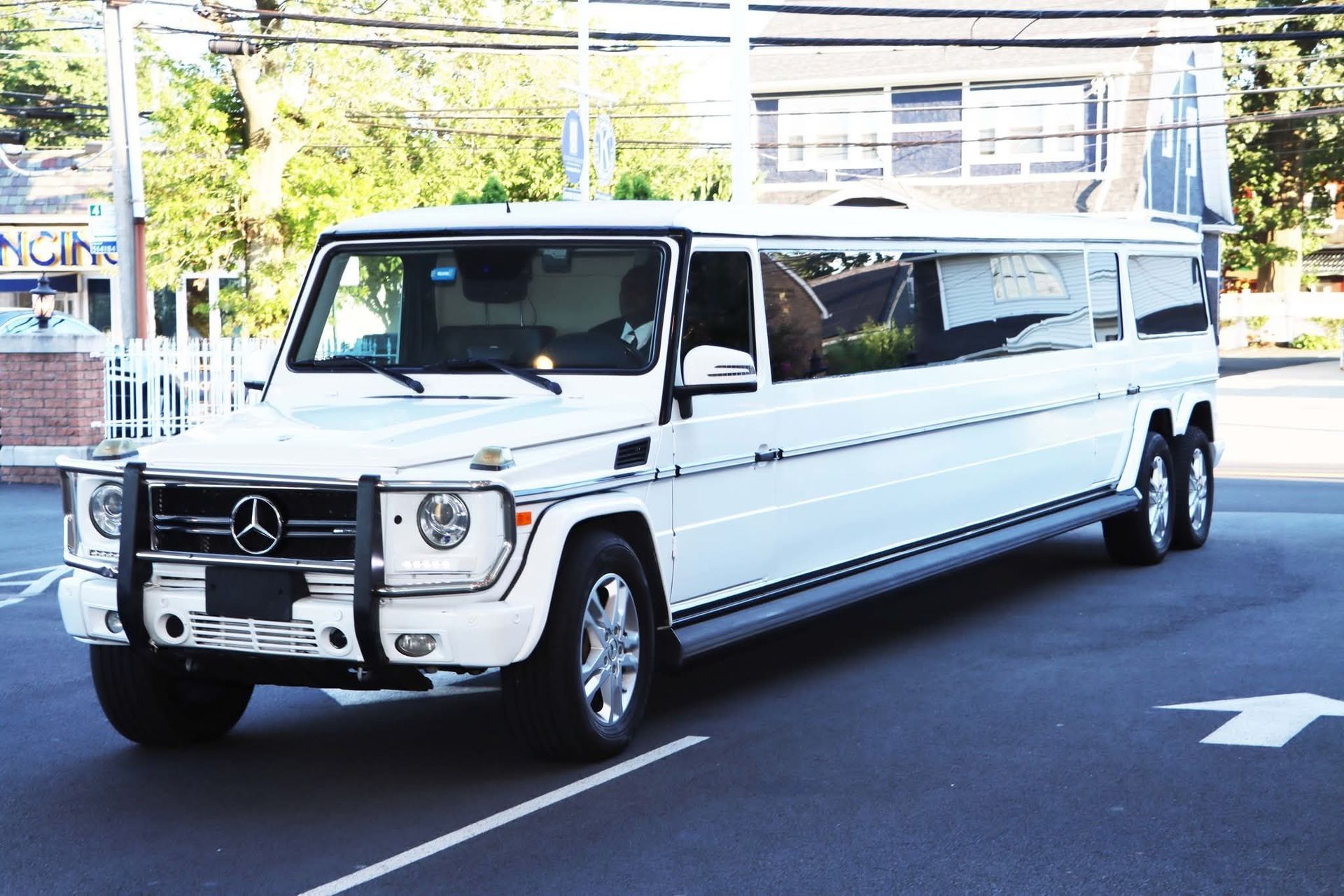 White Mercedes G-Wagon limousine parked on asphalt road in front of building.