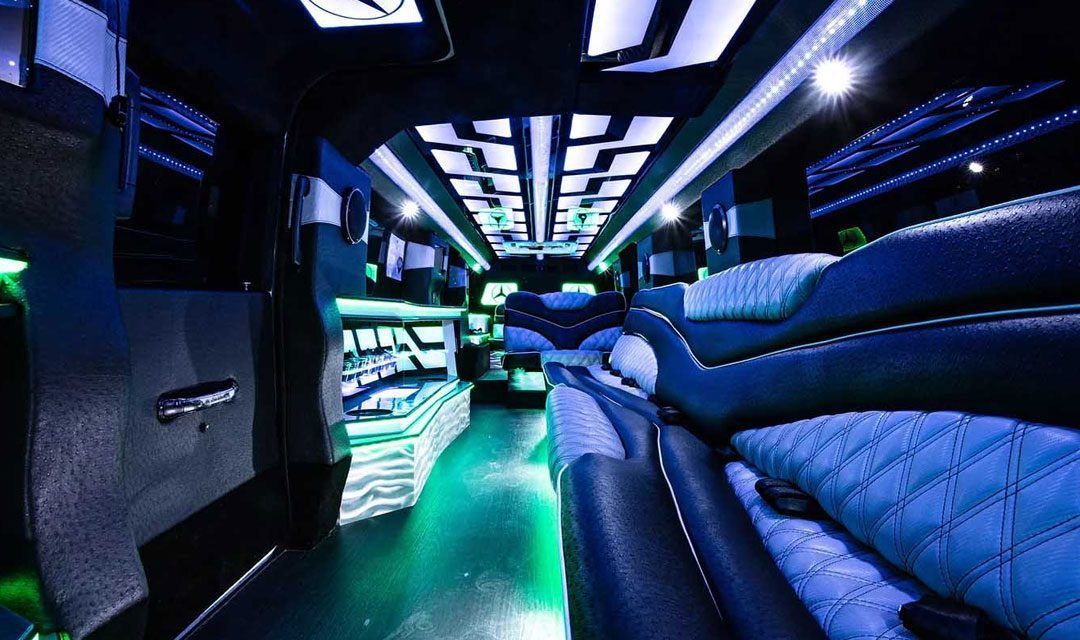Interior of a limousine with blue and green lighting, black seats and a modern design.