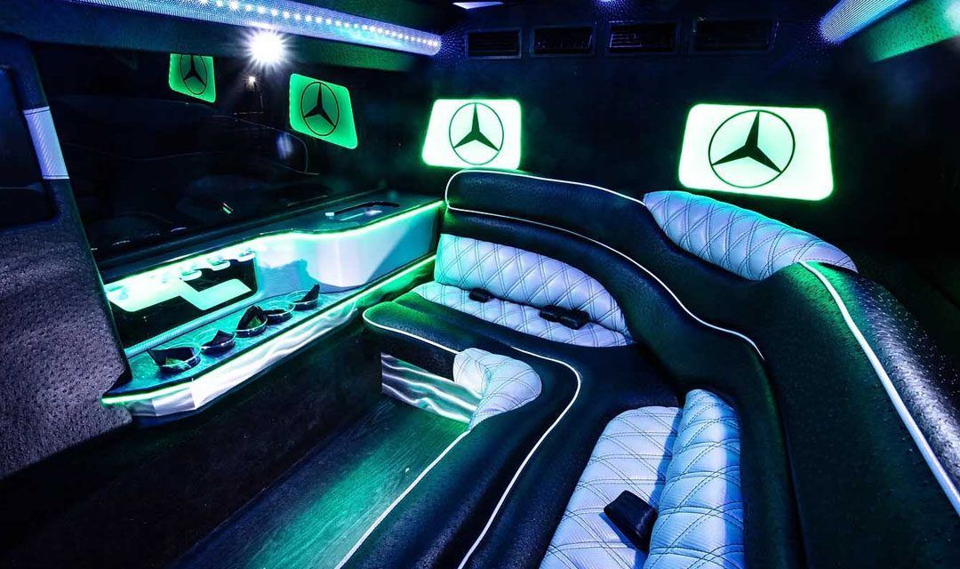 Interior of a party limousine with blue and green neon lights, seating, and screens.