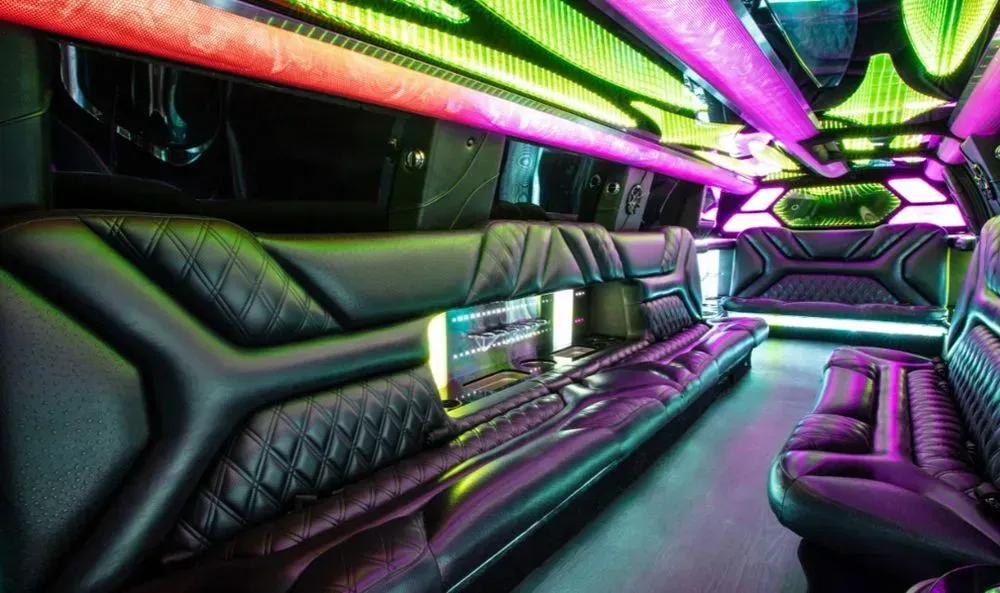 Interior of a limousine with black leather seating, colorful LED lights on ceiling, and cup holders.
