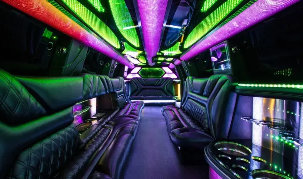 Interior of a limousine with black leather seats, neon lights, and cup holders.