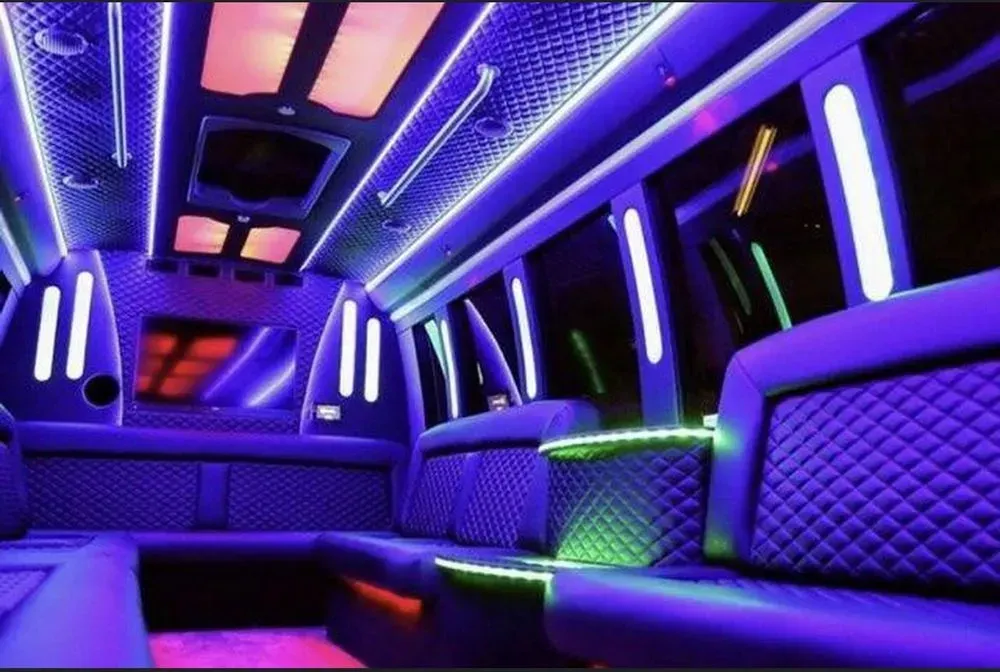 Interior of a party bus with purple and green neon lights illuminating quilted seating and ceiling.