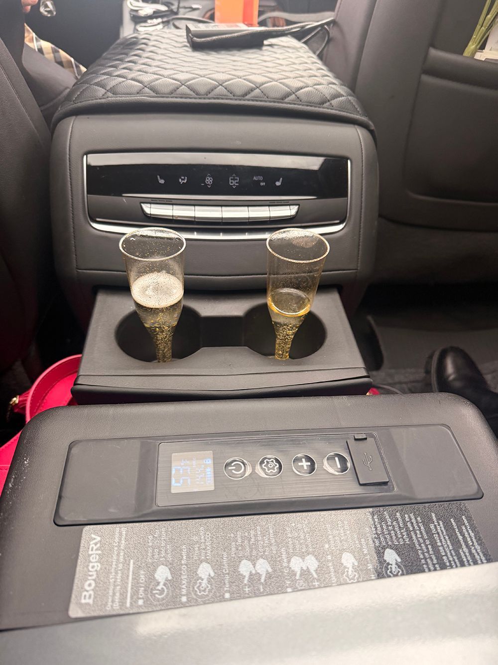 Two champagne flutes in a car's cupholders, near air vents and a power outlet.