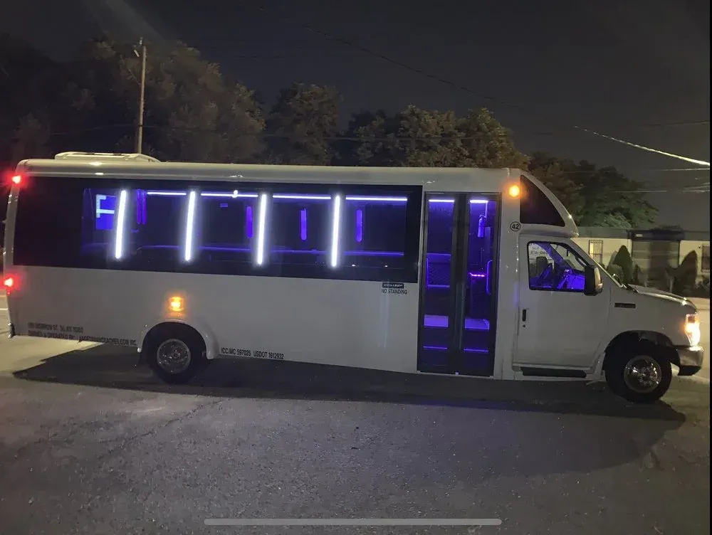 Interior of a party bus with black leather seating, neon lights, and a decorative ceiling.