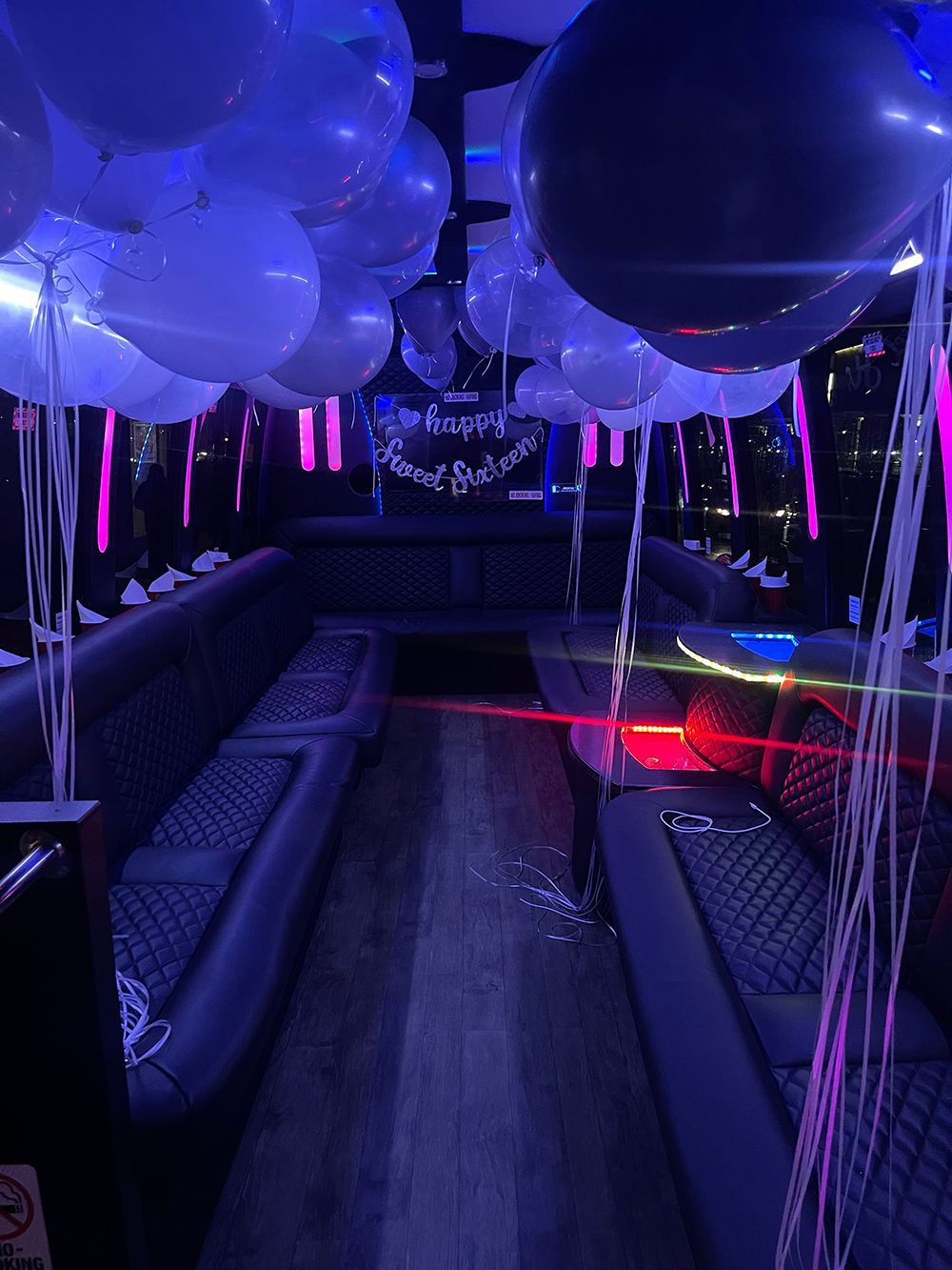 Interior of a party bus decorated with white and black balloons, with a birthday banner.