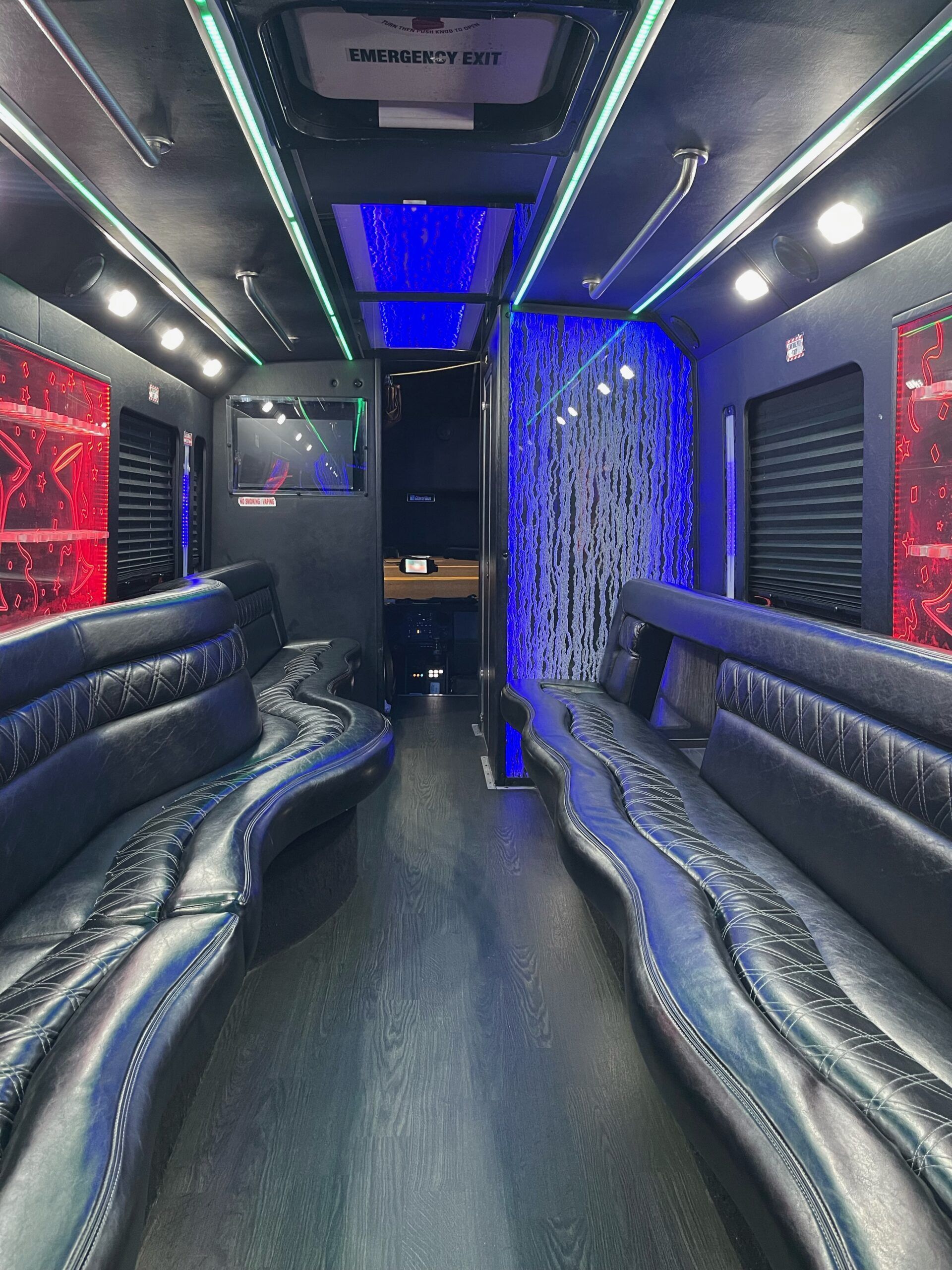 Interior of a party bus with black leather seating, colorful LED lighting, and dark walls.