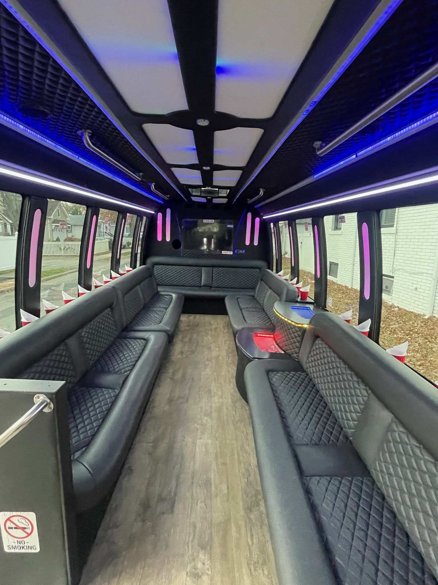 Interior of a party bus with black quilted leather seating, wood-look floor, and blue and white lights.