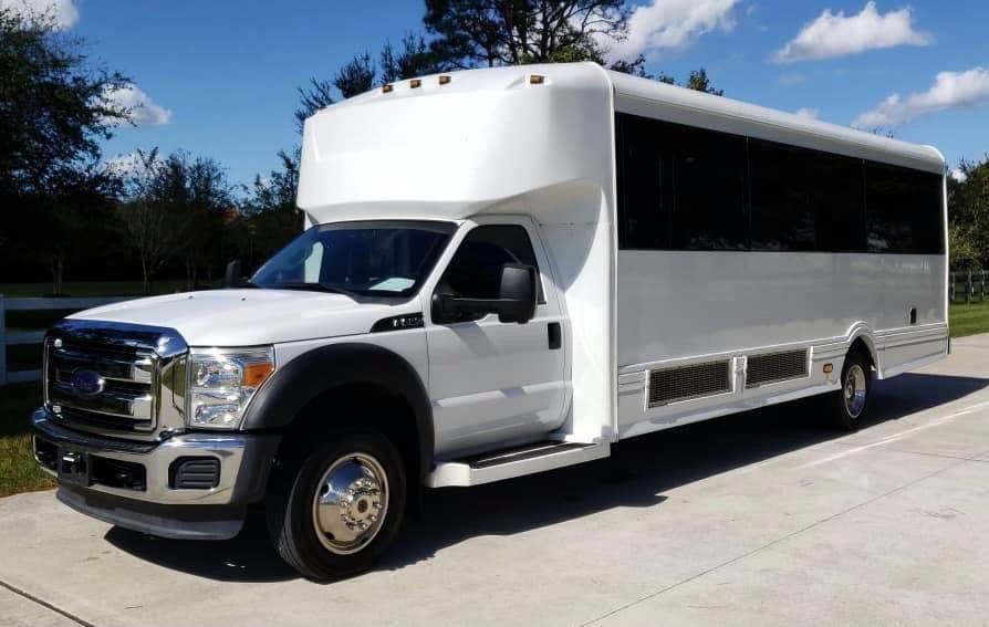 White shuttle bus on asphalt, parked outside on a sunny day.