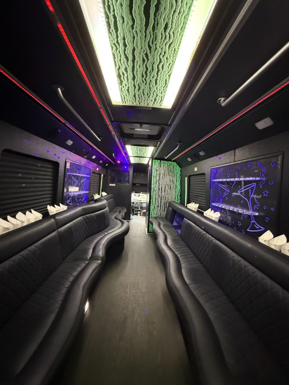 Interior view of a black party bus with leather seating, neon lights, and a decorative ceiling.