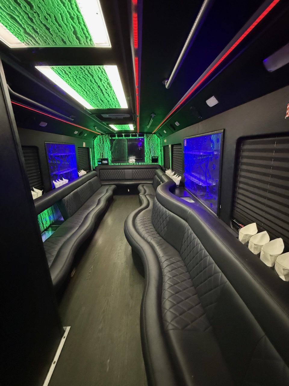 Interior view of a limousine with black leather seating, colorful LED lights on the ceiling, and tinted windows.