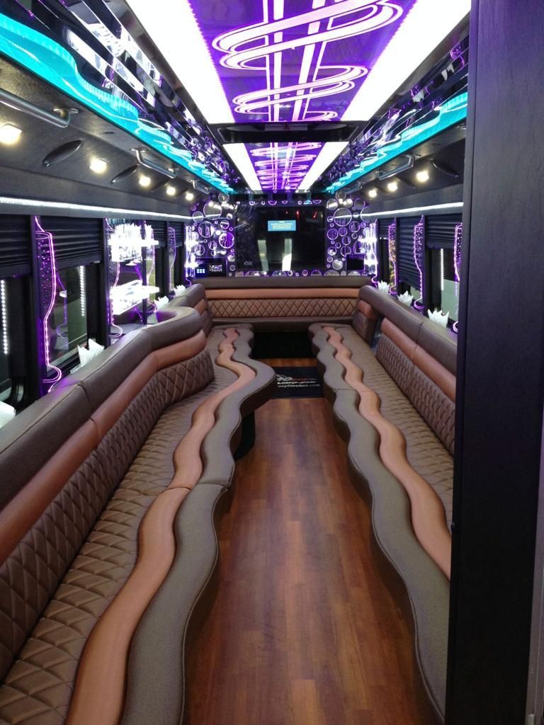 Inside a luxury party bus with brown, gray, and pink seating, a wood floor, and purple lighting.