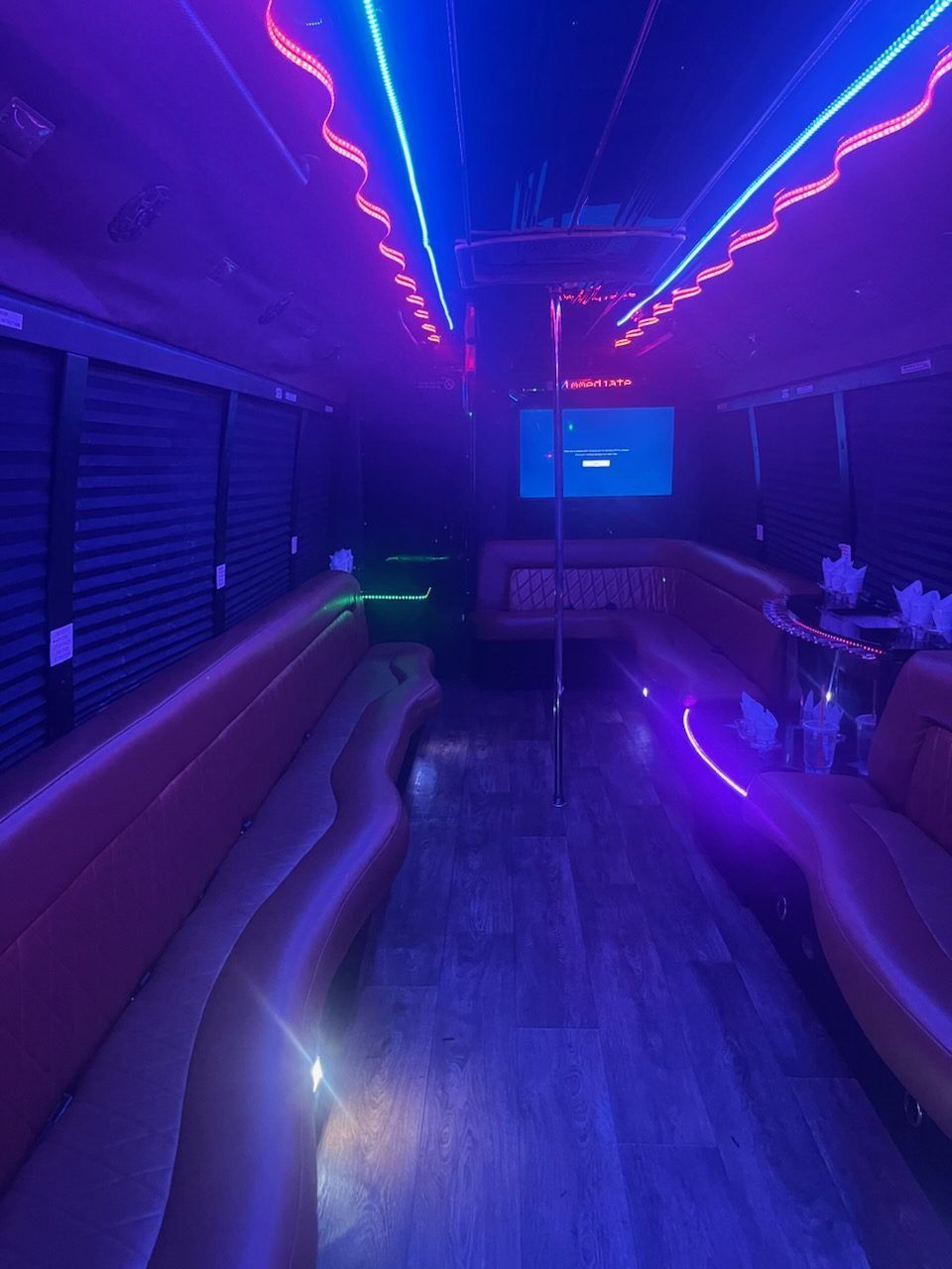 Inside a party bus with neon lights and a pole.