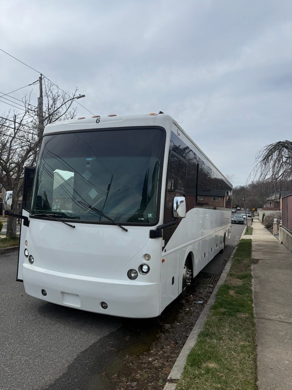 White passenger bus parked on a street next to a sidewalk. Gray sky overhead.