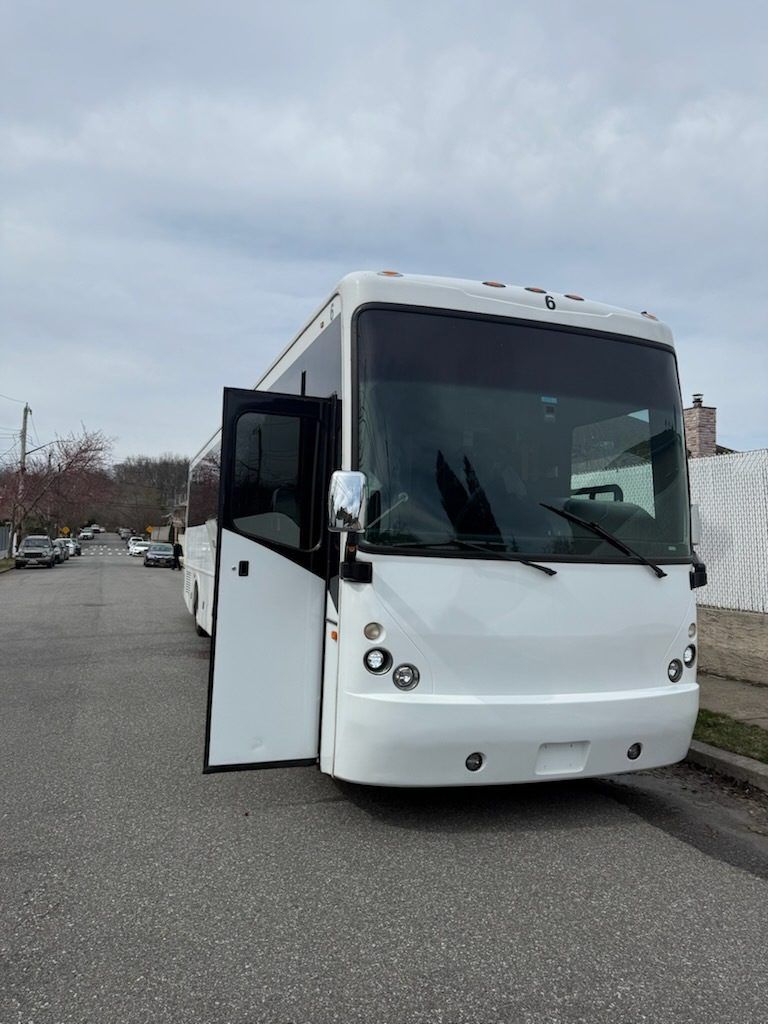 White tour bus parked on a city street, door open, overcast sky.