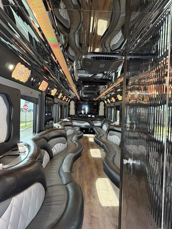 Interior of a luxury party bus with black and gray seating, shiny black ceiling, and wood-look flooring.