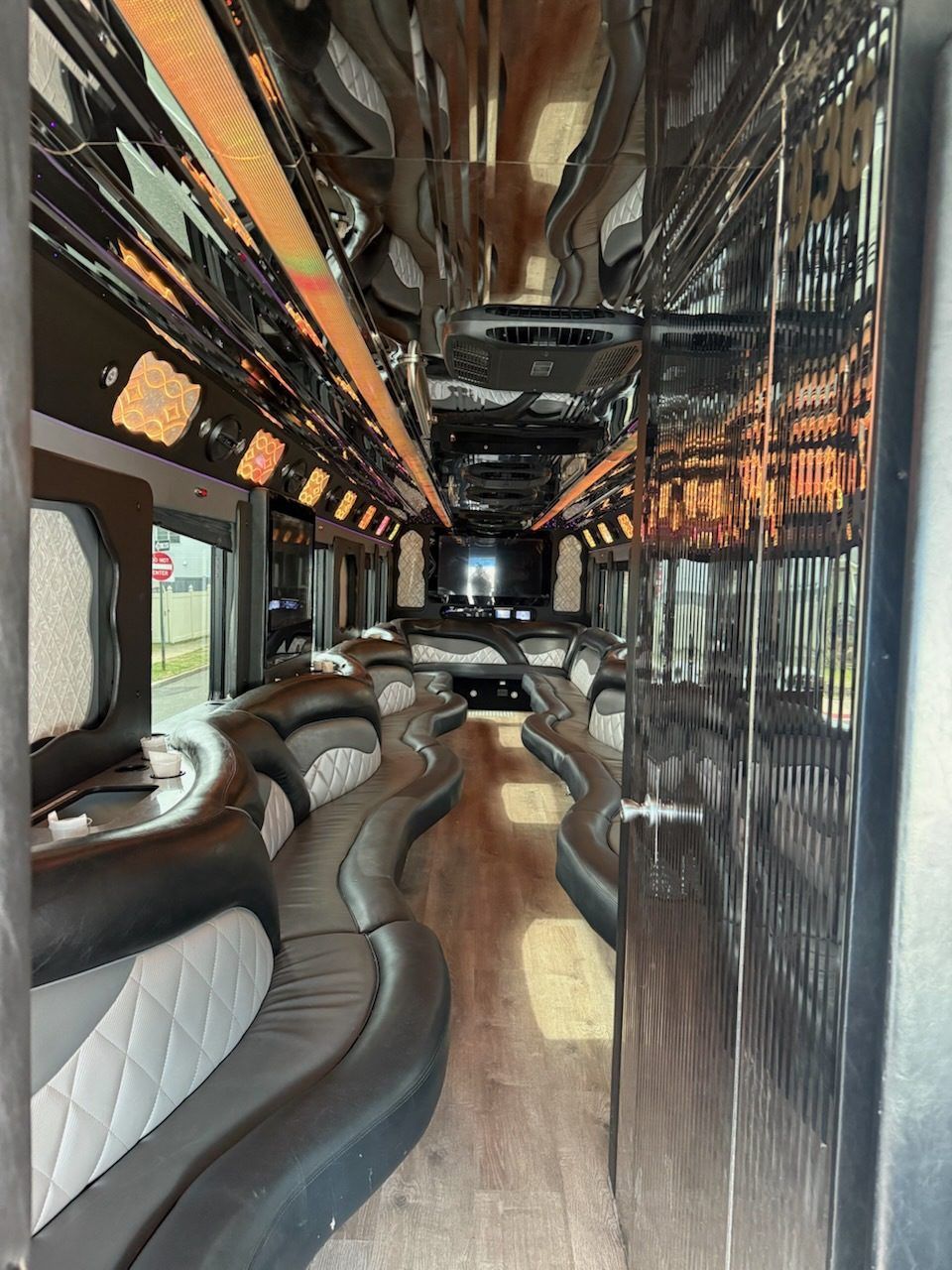 Interior of a party bus with black and silver seating, mirrored ceiling, and wood flooring.