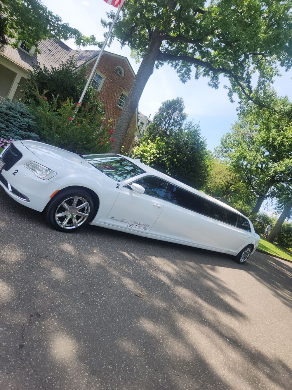 White Chrysler limousine parked on a driveway with a tree in the background. An American flag is visible.