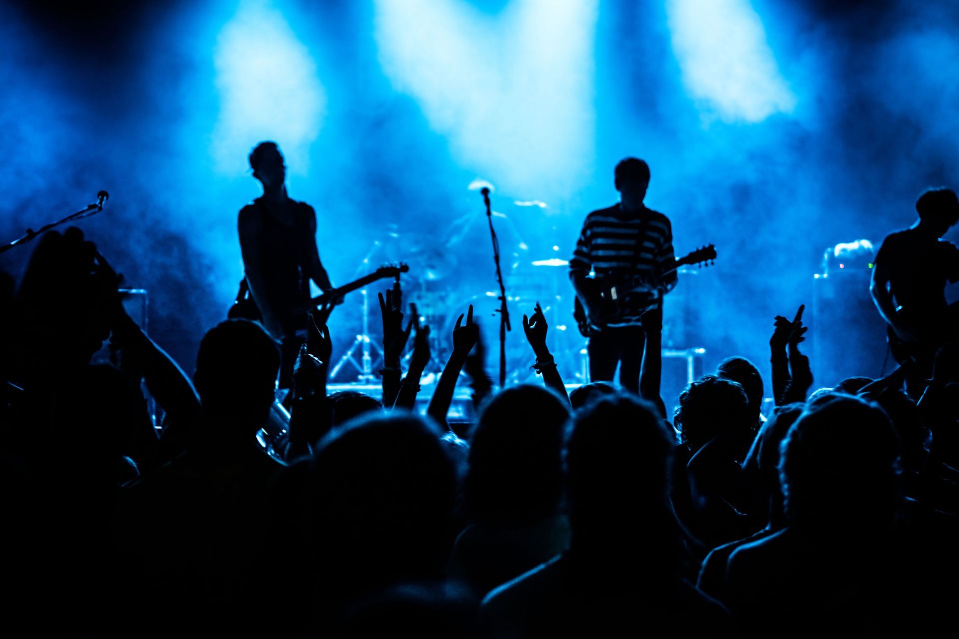 Band performing on stage under blue lights; crowd with raised hands.