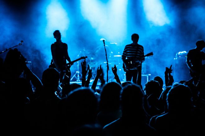 Band performing on stage under blue lights; crowd with raised hands.