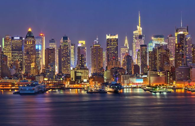 Night skyline of New York City, illuminated buildings reflected in the dark water.