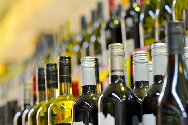 Wine bottles lined up on a shelf, various colors and styles.