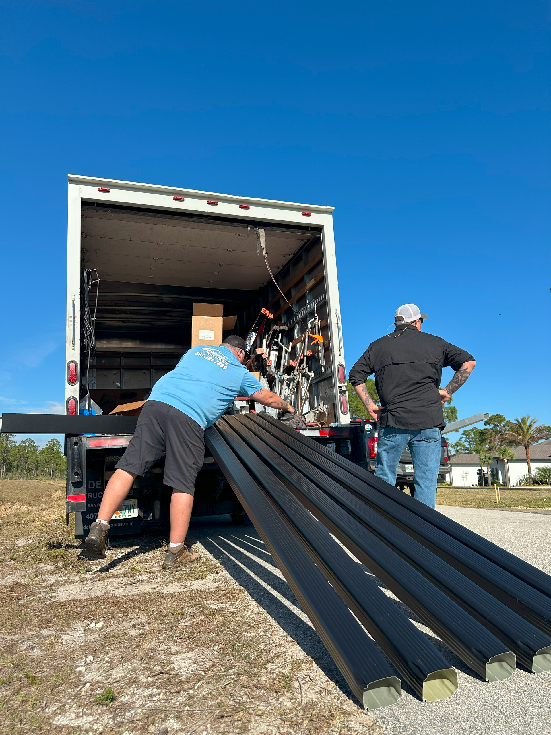 Two men are loading a truck with a stack of black pipes.