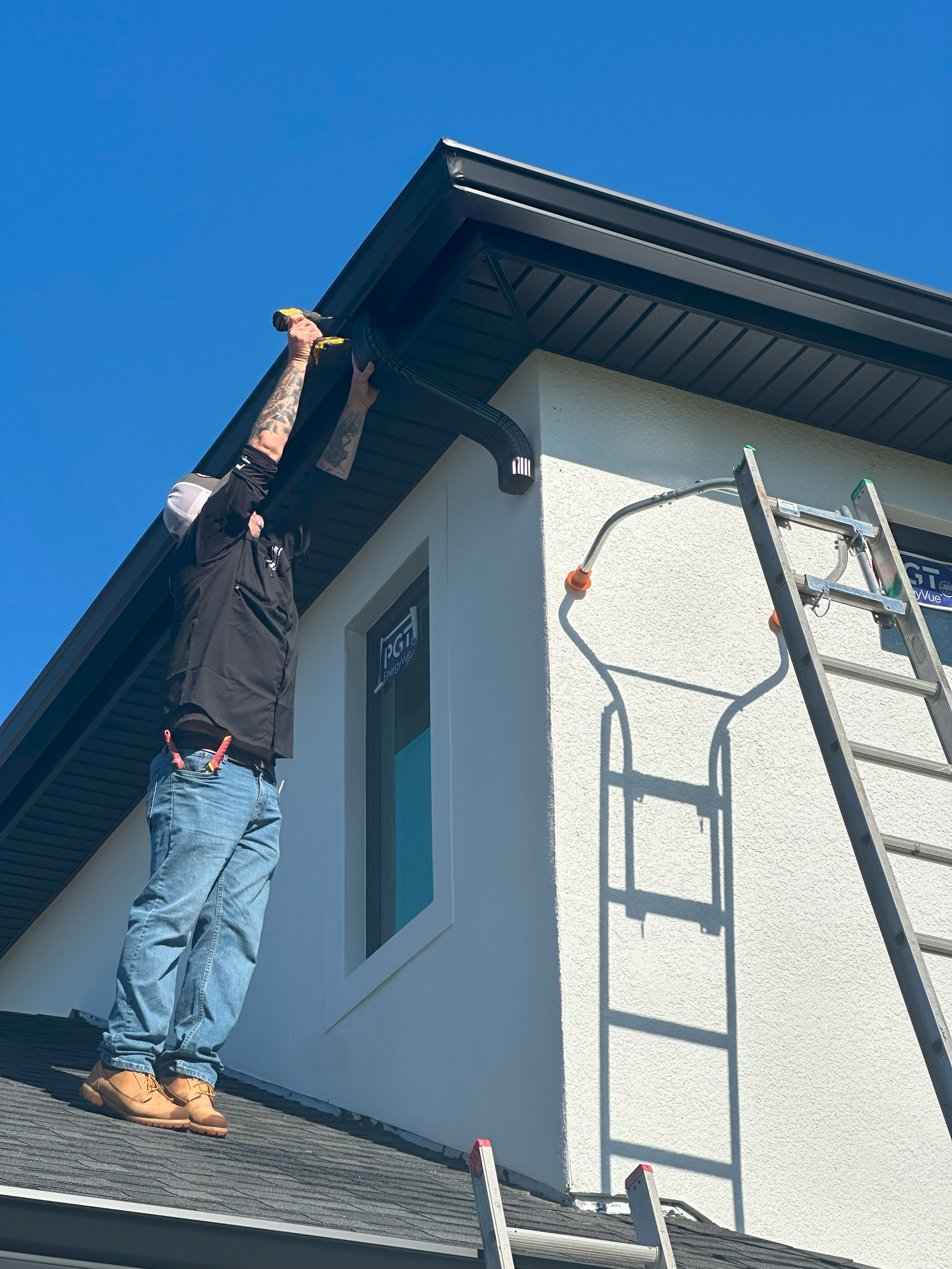 A man is standing on the roof of a house with a ladder.