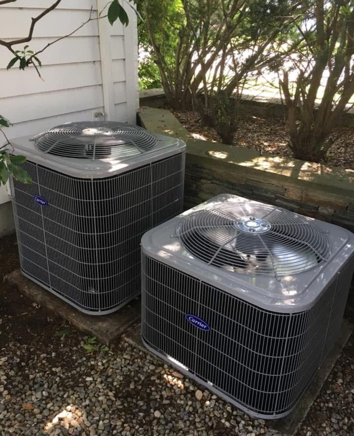 Two air conditioners are sitting next to each other outside of a house.