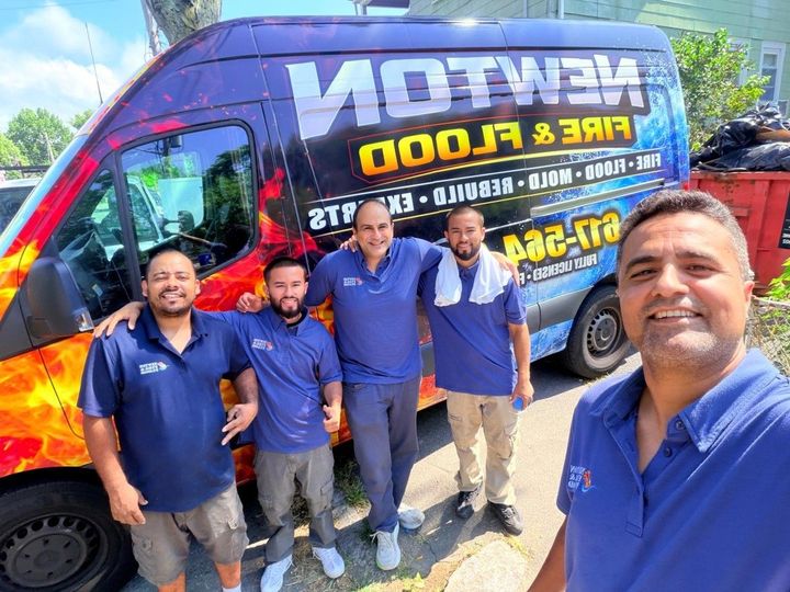 Five men in blue shirts posing beside a branded van on a sunny street.