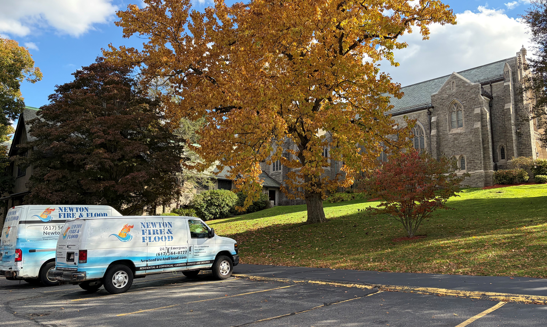 Two service vans parked near a stone building and fall foliage on a sunny day.