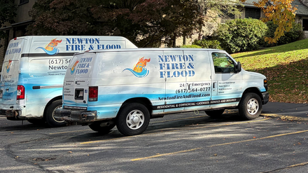 Two service vans parked near a building with autumn trees.