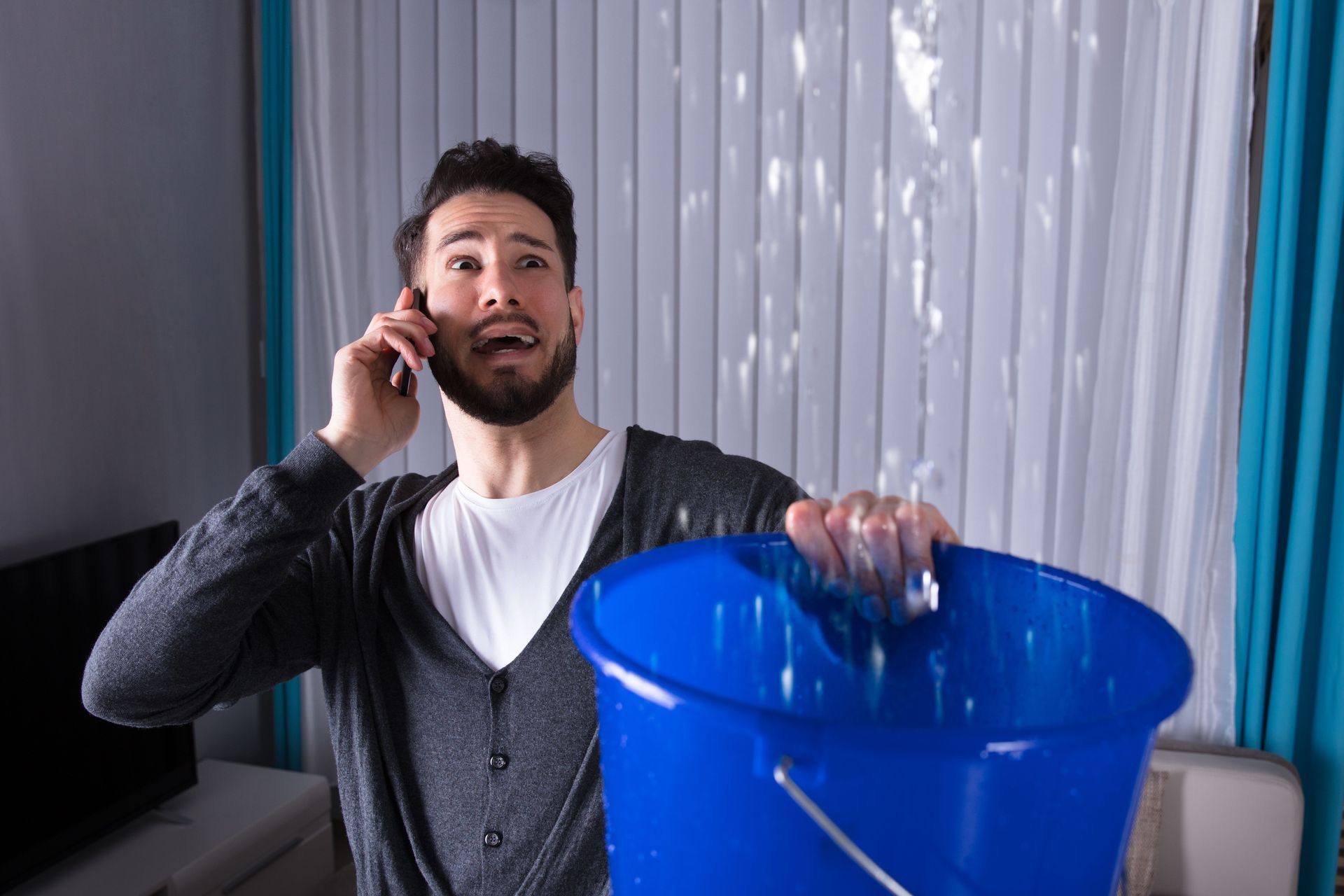 Man on phone holding blue bucket indoors beside a white curtain