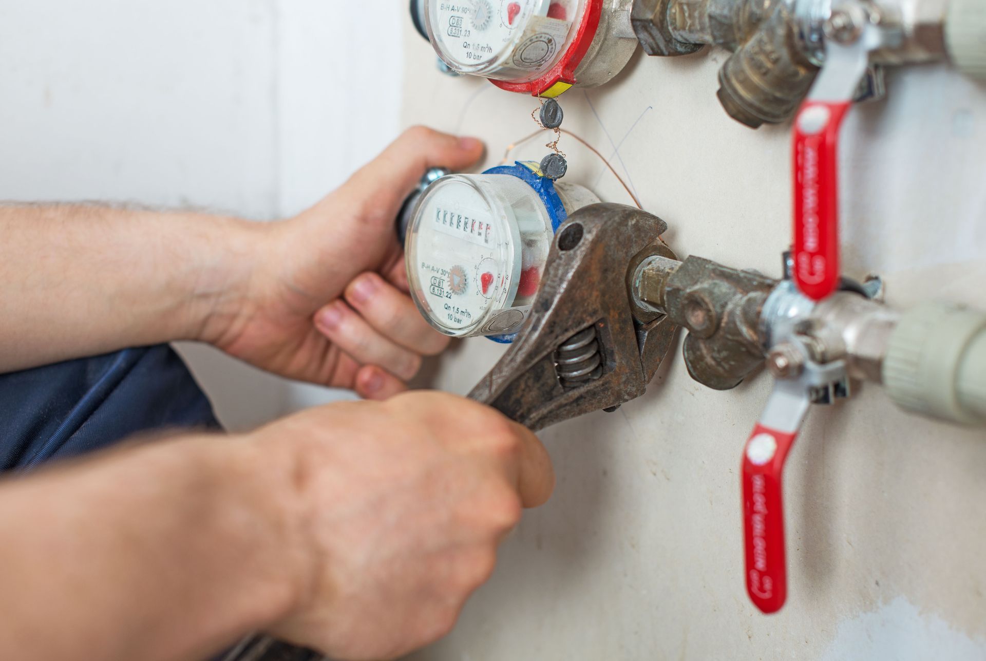 Hands adjusting a water meter with a wrench beside red-handled pipes