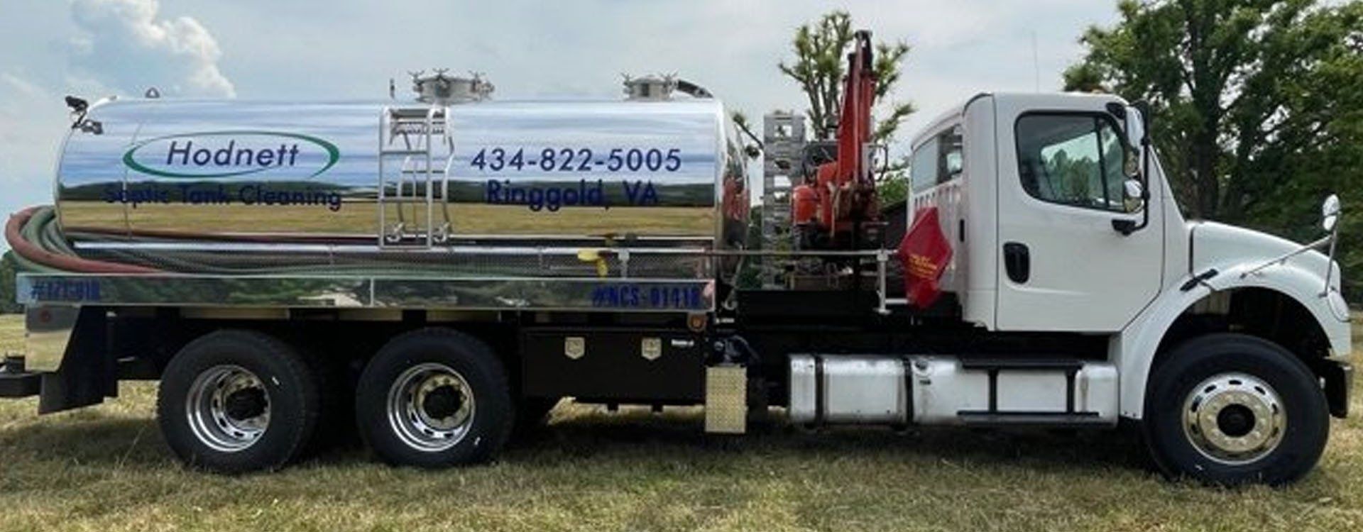White septic truck with a silver tank, parked on a grassy area. Hodnett logo and phone number on the tank.